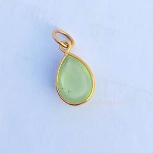 May include: A gold pendant with a light green gemstone in the shape of a teardrop.
