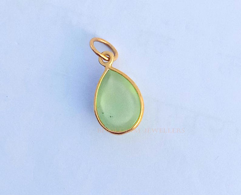 May include: A gold pendant with a light green gemstone in the shape of a teardrop.