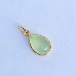 May include: A gold pendant with a light green teardrop-shaped gemstone.