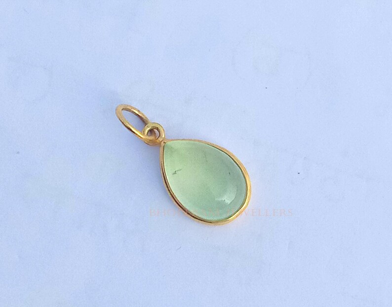 May include: A gold pendant with a light green teardrop-shaped gemstone.