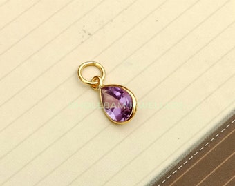 Puede incluir: Un colgante de oro con una piedra preciosa de amatista púrpura en forma de lágrima.