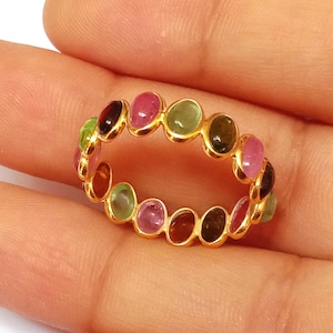 May include: A gold ring with a band of oval-shaped gemstones in various colors, including pink, green, and brown.