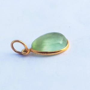 May include: A teardrop-shaped green gemstone pendant with a gold setting.