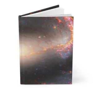 Op de afbeelding: Een hardcover journal met een kleurrijk galaxy-ontwerp op de omslag. De galaxy is een wervelende mix van rode, oranje, gele en blauwe tinten.