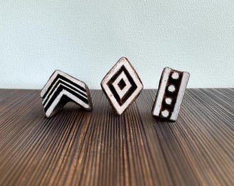 May include: Three wooden printing blocks with geometric designs. The blocks are black and white and have a diamond, a chevron, and a dotted line pattern.