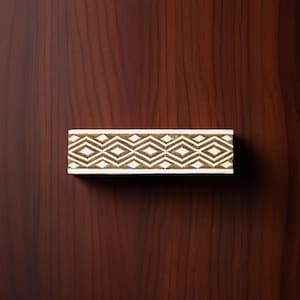 May include: A white wooden printing block with a carved geometric pattern of brown diamonds.
