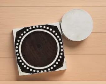 Peut inclure: Un carreau décoratif carré noir et blanc avec un motif circulaire et une bordure pointillée, à côté d'un carreau rond blanc. Les carreaux sont sur une surface en bois brun clair.