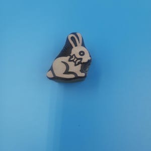May include: A wooden stamp with a black outline of a white rabbit wearing a bow tie. The rabbit is sitting on its hind legs with its ears up.