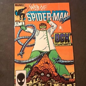 May include: A comic book cover featuring Spider-Man in a red and blue suit, fighting Doctor Octopus, who is wearing a green and white lab coat and has four mechanical arms. The cover is orange with the text "Web of Spider-Man" and "Doc Ock Triumphant!" in black.
