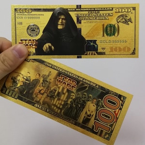 May include: A gold-coloured paper bill with a Star Wars theme. The front features Darth Vader, the text "GOLD 999999", and the words "Star Wars". The back features a scene from Star Wars with the text "Star Wars" and "One Hundred Dollars".