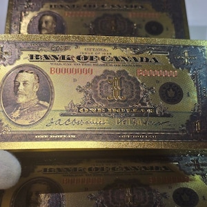 May include: Gold-colored Canadian one-dollar bill from 1938. The bill features a portrait of a man and the text "The Bank of Canada". The bill is rectangular and has intricate designs and text.