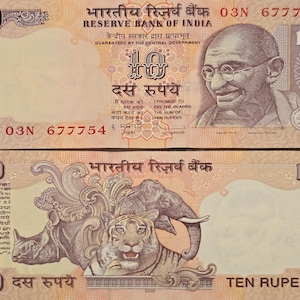 May include: A 10 rupee Indian banknote featuring a portrait of Mahatma Gandhi on the front and a depiction of a tiger, rhinoceros, and elephant on the back. The banknote is in good condition and has the text "भारतीय रिज़र्व बैंक" (Reserve Bank of India) printed on it.