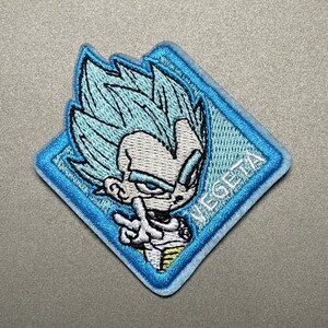 May include: Blue and white embroidered iron-on patch featuring a cartoon character with spiky blue hair and the word "VEGETA" in white text.