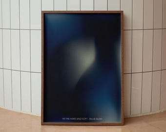 May include: A framed print featuring an abstract design in shades of blue and white. The text "HIT ME HARD AND SOFT - BILLIE EILISH" is printed at the bottom of the print.