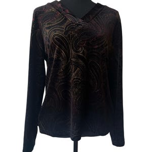 May include: A long-sleeved, dark-colored top with a V-neck and a paisley pattern. The fabric appears to be velvet, with gold and burgundy accents. The top is displayed on a black mannequin.