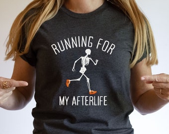 May include: Dark grey heather t-shirt with the text "RUNNING FOR MY AFTERLIFE" and a running skeleton graphic. The skeleton is wearing orange shoes. A humorous tee for Halloween or a fun gift.