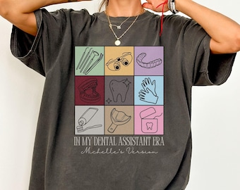 May include: A dark grey t-shirt with a graphic design of dental tools and the text "In My Dental Assistant Era Michelle's Version".