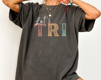 May include: A black oversized t-shirt with the text "Let's TRI" in colorful retro-style lettering.
