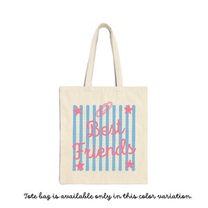 May include: A beige canvas tote bag featuring a central graphic of vertical light blue stripes. Overlaid on the stripes is the pink text "Best Friends" in a cursive script, accompanied by a pink paperclip icon and four pink stars.