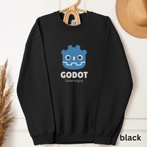 May include: Black sweatshirt with a blue Godot game engine logo. The logo features a cartoon robot head with gears and a friendly face.