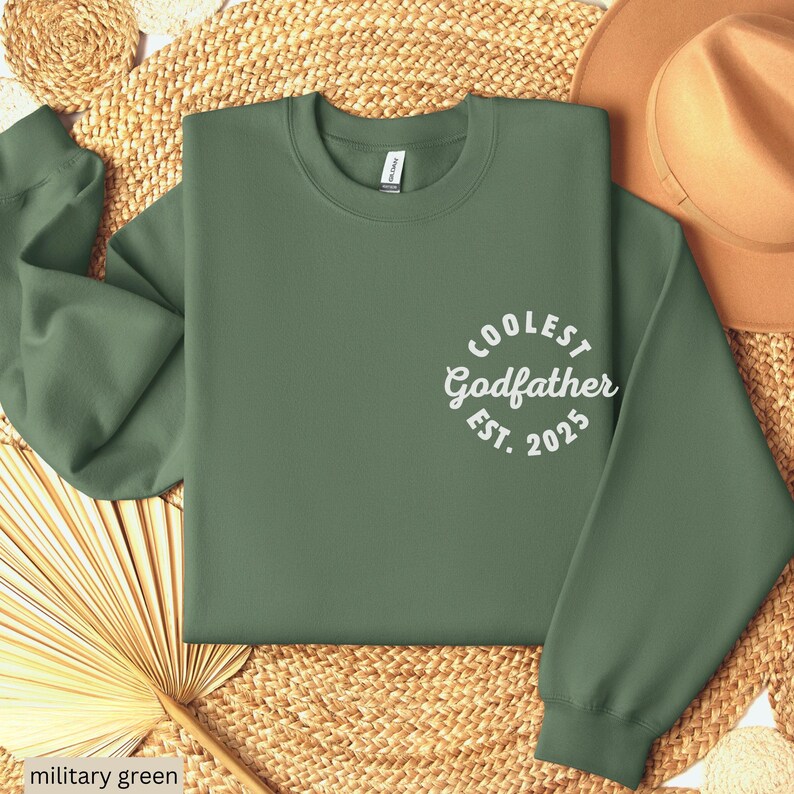 May include: A military green sweatshirt with the text "Coolest Godfather Est. 2025" in white.