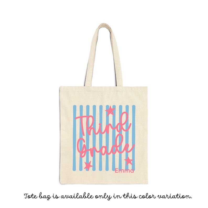 May include: A beige canvas tote bag featuring a vertical light blue striped pattern. The text "Third Grade" is printed in a pink script font, accompanied by three small pink stars and the name "Emma" in a simple pink sans-serif font.