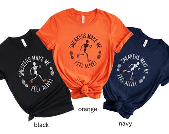 May include: Three short-sleeve crew neck t-shirts in black, orange, and navy blue. Each shirt features a graphic of a running skeleton with the text "SNEAKERS MAKE ME FEEL ALIVE!" arranged in a circle around the skeleton, accompanied by two sneaker footprints.