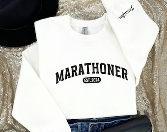 May include: White sweatshirt with black text that reads "MARATHONER EST. 2024". The sweatshirt has a crew neck and long sleeves.