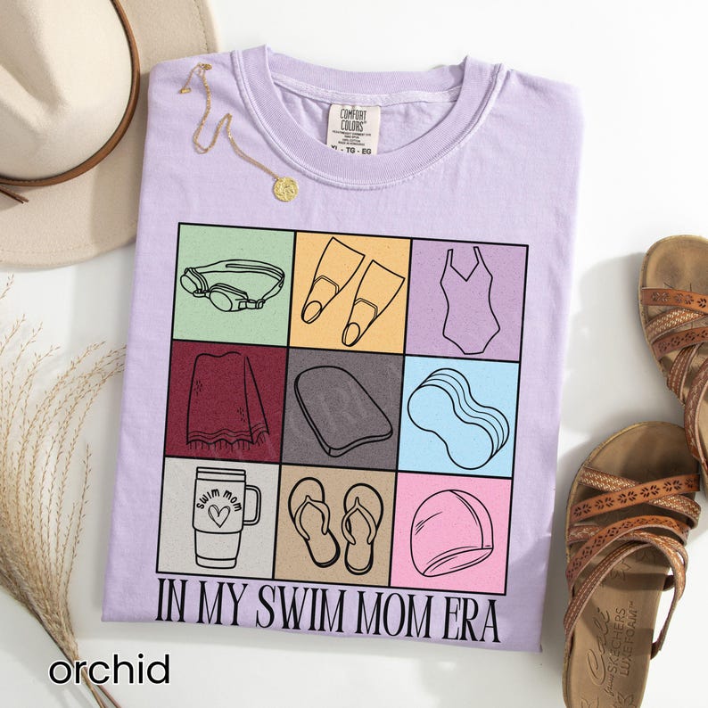 May include: A light purple t-shirt featuring a grid of nine squares, each containing a black line drawing of swimming gear including goggles, fins, a swimsuit, a towel, a kickboard, a pool noodle, a tumbler, flip-flops, and a swim cap, with the text "IN MY SWIM MOM ERA" printed below.