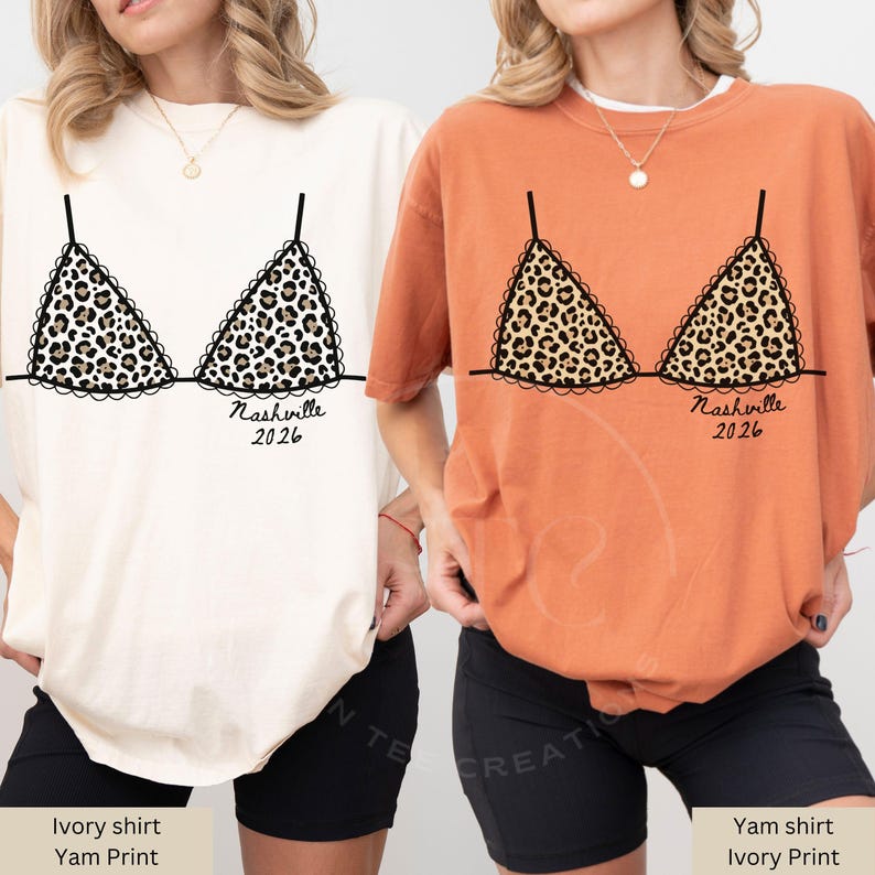 May include: Two t-shirts, one ivory and one yam-colored, each featuring a leopard print bra design. The design includes the text "Nashville 2026" in black script. The shirts are casual and comfortable.