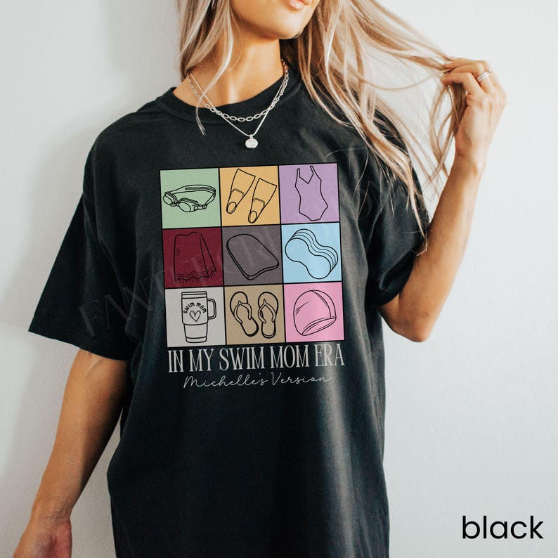 May include: A black t-shirt featuring a grid of nine colorful squares containing line art icons of swimming gear, including goggles, fins, a swimsuit, a towel, a kickboard, a noodle, a tumbler, flip-flops, and a cap, with text reading IN MY SWIM MOM ERA and Michelle's Version.