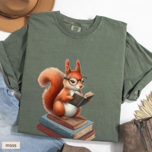 May include: A green t-shirt with a cartoon image of a squirrel wearing glasses and reading a book. The squirrel is sitting on a stack of books.