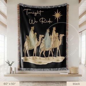 May include: A black woven throw blanket featuring the text Tonight We Ride in gold script, a gold star, and three figures wearing crowns and robes riding camels across a desert landscape. The blanket has a fringed edge and measures 60 by 50 inches.