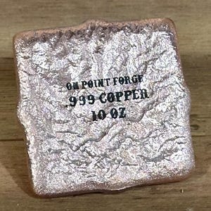 K&ouml;nnte beinhalten: Eine strukturierte, rechteckige Kupferbarren mit dem Text "ON POINT FORGE 999 COPPER 10 OZ" auf der Vorderseite. Der Barren hat eine raue, unebene Oberfl&auml;che und eine metallische, rosafarbene Silberfarbe.