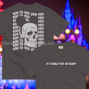 Może przedstawiać: Ciemnoszary t-shirt z krótkim rękawem z białą grafiką czaszki otoczoną powtarzającym się tekstem "BOO TO YOU AND YOU" na plecach oraz napisem "IT'S REALLY NOT SO SCARY" wydrukowanym na biało z przodu na klatce piersiowej.
