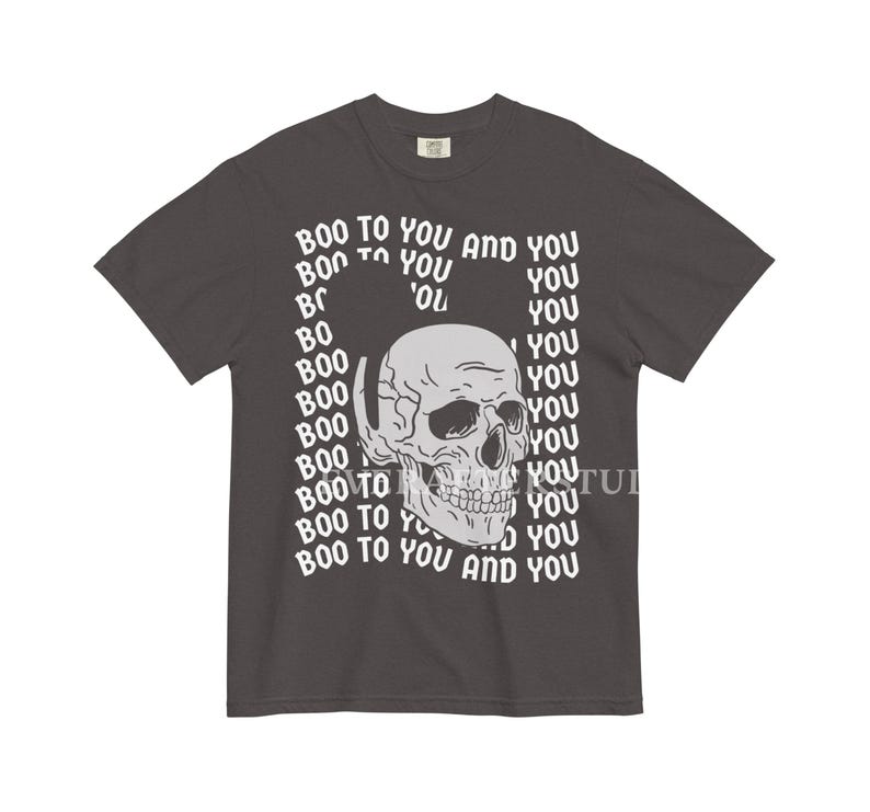 Może przedstawiać: Ciemnoszary t-shirt z kr&oacute;tkim rękawem z centralną grafiką jasnoszarej ludzkiej czaszki. Wz&oacute;r otoczony jest powtarzającym się białym napisem "BOO TO YOU AND YOU", ułożonym w falisty, prostokątny wz&oacute;r na wysokości klatki piersiowej.