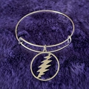 May include: A silver bangle bracelet with a circular charm featuring the iconic Grateful Dead lightning bolt logo.