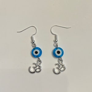 May include: A pair of silver earrings with blue evil eye charms and silver Om symbols hanging from them.