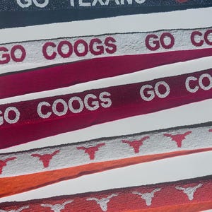 May include: Close-up of several beaded belts with team-themed designs. One belt reads "GO TEXANS" with a football graphic. Other belts feature "GO COOGS" and longhorn symbols. The belts are in various colors, including navy, red, and orange.
