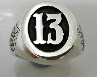 Può includere: Un anello d'argento con un cerchio nero al centro. Il numero "13" è scritto in bianco all'interno del cerchio.