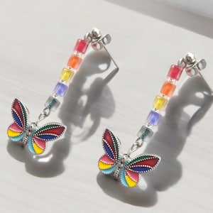 May include: Rainbow colored glass bead dangle earrings with a silver butterfly charm. The butterfly has a multi-colored enamel design.