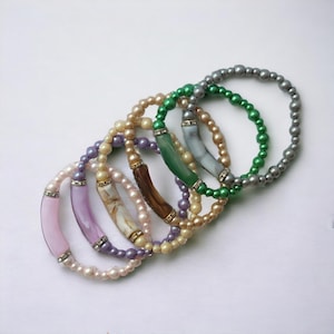May include: A set of six beaded bracelets with different colored beads and decorative accents. The bracelets feature a variety of colors, including green, purple, and white.