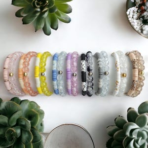 May include: A set of ten colorful beaded bracelets with crystal accents. Each bracelet features a different color and pattern, including yellow, pink, blue, gray, and black.