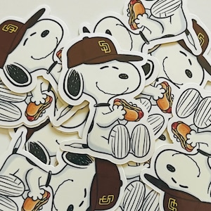 May include: A collection of white stickers featuring a cartoon dog wearing a brown baseball cap with a brown logo and eating a hot dog. The stickers have a white border and are scattered across a white surface.