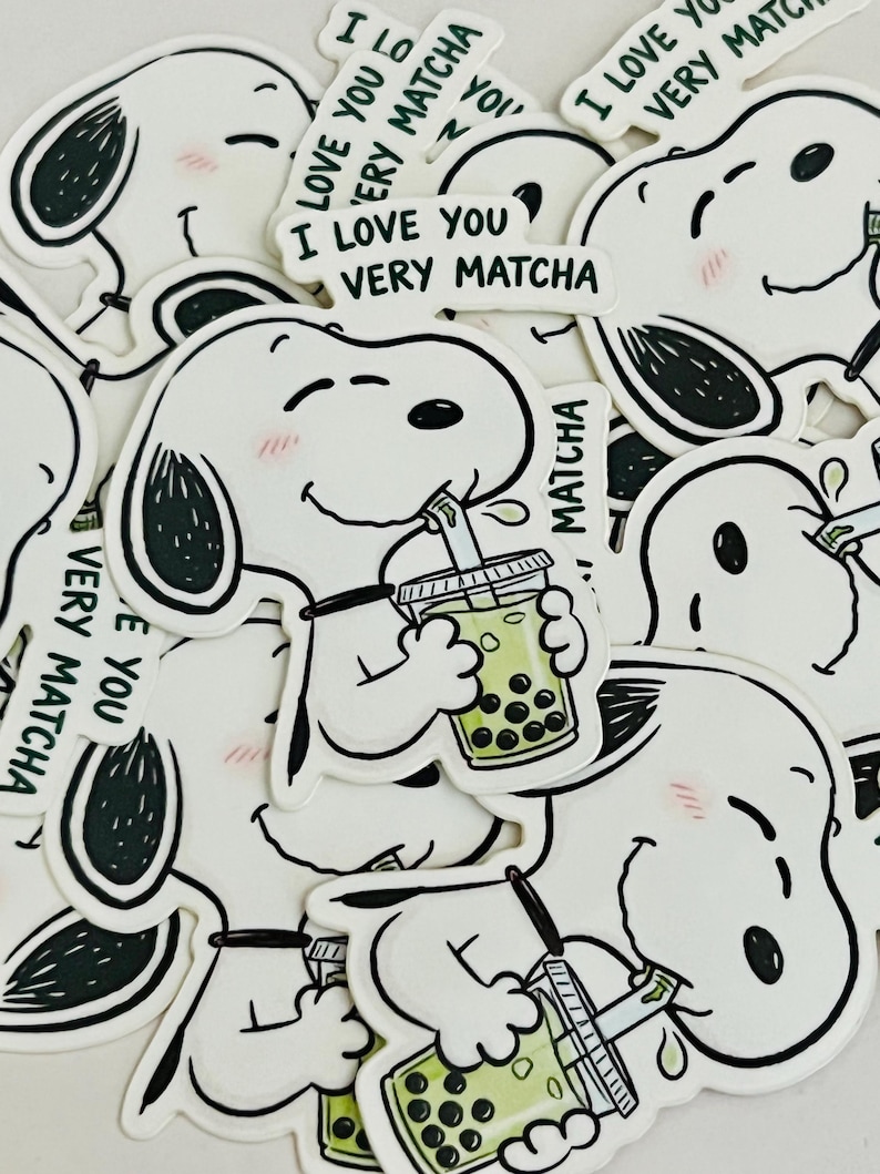 Pode incluir: Autocolantes brancos com um c&atilde;o de desenho animado com orelhas pretas e bochechas rosadas, bebendo ch&aacute; de bolhas. Os autocolantes t&ecirc;m o texto "I LOVE YOU VERY MATCHA" em verde.