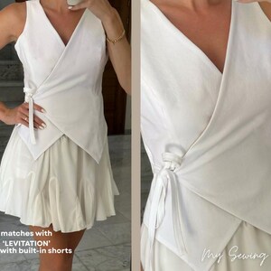May include: A white wrap top with a V-neck and tie closure, paired with a matching skirt. The skirt has a layered, ruffled design. The outfit is a monochromatic ensemble, perfect for a summer look. The text on the image says "matches with 'LEVITATION' skirt with built-in shorts".