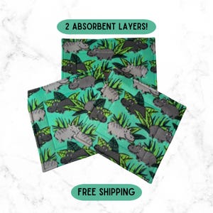 May include: Three square fabric pads featuring a repeating pattern of grey hippos and green jungle leaves on a bright teal background. The top pad includes a green oval label with the text 2 ABSORBENT LAYERS! in black capital letters.