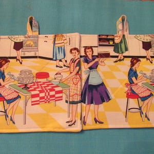 May include: A set of two white cotton pot holders with a retro kitchen theme. The pot holders feature a checkered pattern in red and white, and a design of women in vintage dresses baking in a kitchen.