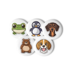 Puede incluir: Cinco botones redondos blancos con ilustraciones de animales de dibujos animados. Los diseños incluyen una rana verde, un pingüino, un perro salchicha, un oso pardo y un beagle. Los botones están dispuestos en un patrón circular.