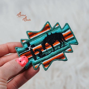 May include: A turquoise, orange, and white striped iron-on patch with a silhouette of a horse and the word "Home" embroidered in black.